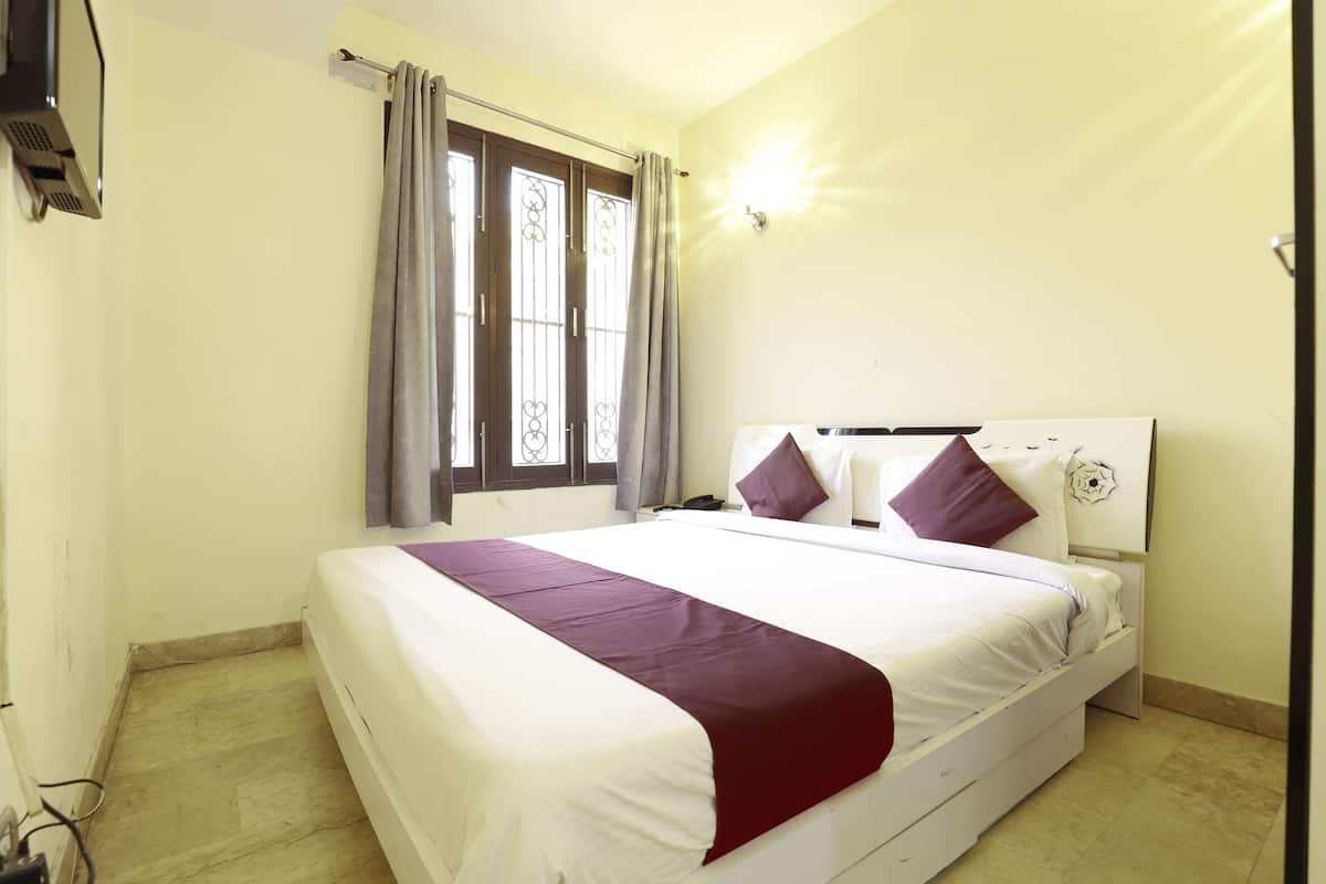 Una habitación de hotel con cama, cortinas, ventana y una lámpara fijada a la pared.