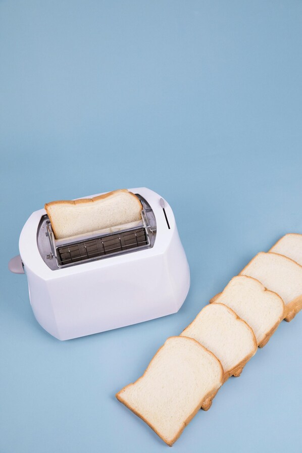 A white toaster with a slice of bread inside, and several slices of white bread on a blue surface. - Livia Residency (New Delhi)