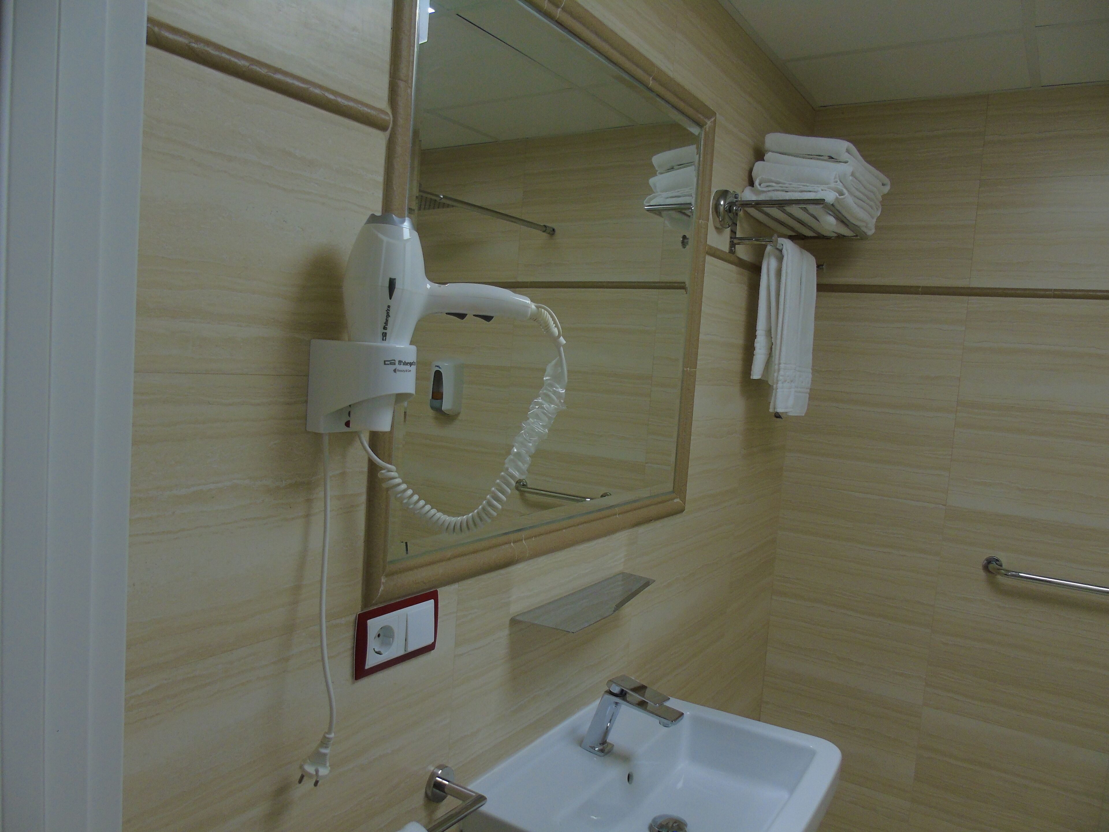 A bathroom with a white sink, a mirror, a hairdryer, and a towel rack.