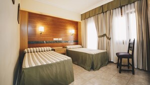 A hotel room with two single beds, a wooden headboard, two bedside lamps, a chair, and a window with curtains. - Hostal Los Gavilanes 2 (Toledo)