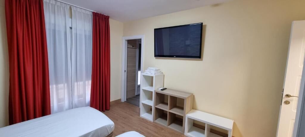 A room with a bed, a TV mounted on the wall, and a small desk with shelves.