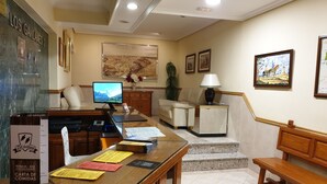 A hotel lobby with a reception desk, a computer monitor, a sofa, a coffee table, and a staircase leading to another floor. - Hostal Los Gavilanes 2 (Toledo)