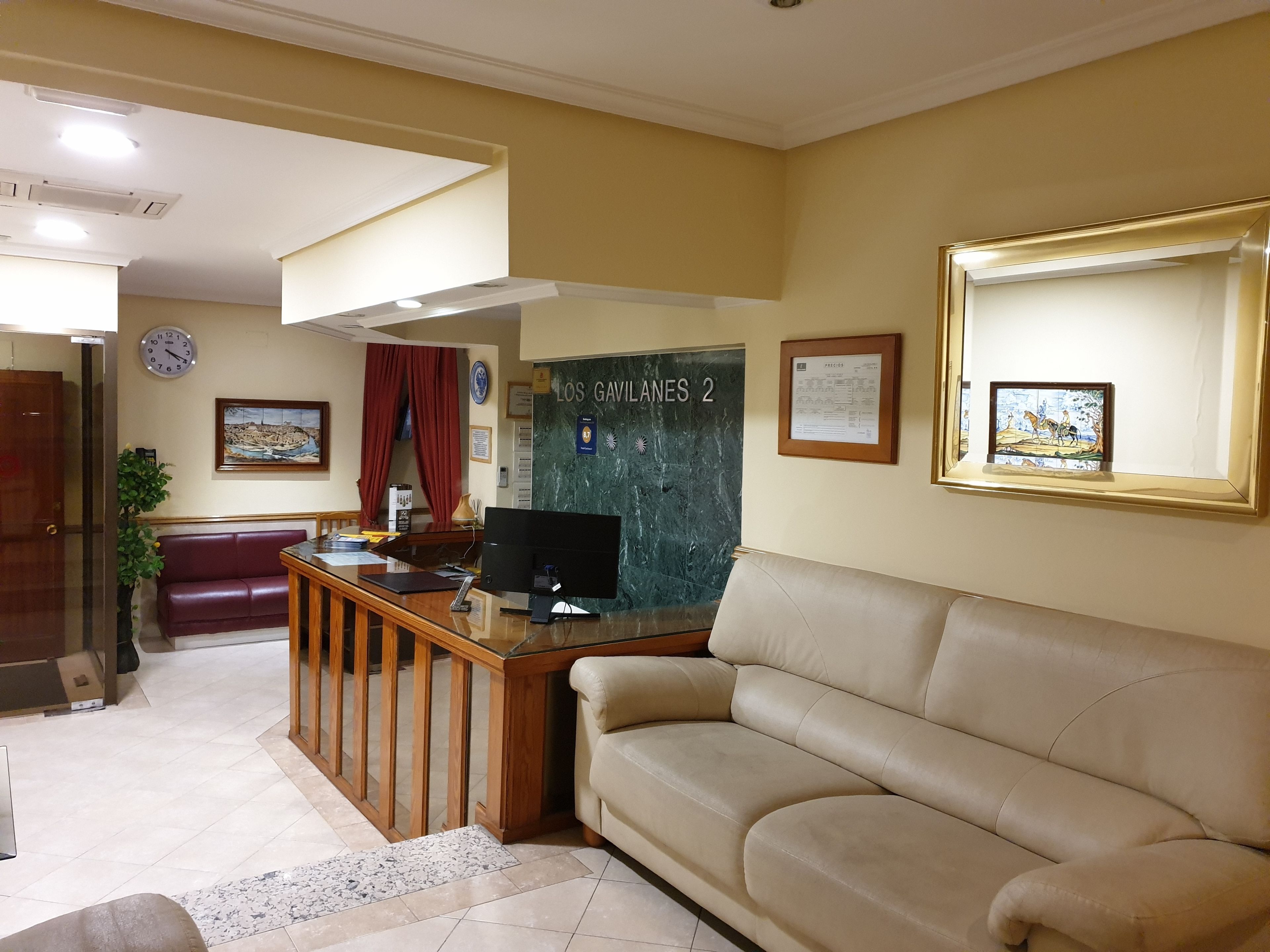 A reception area with a desk, computer, and a couch. A clock and a framed picture are on the wall.