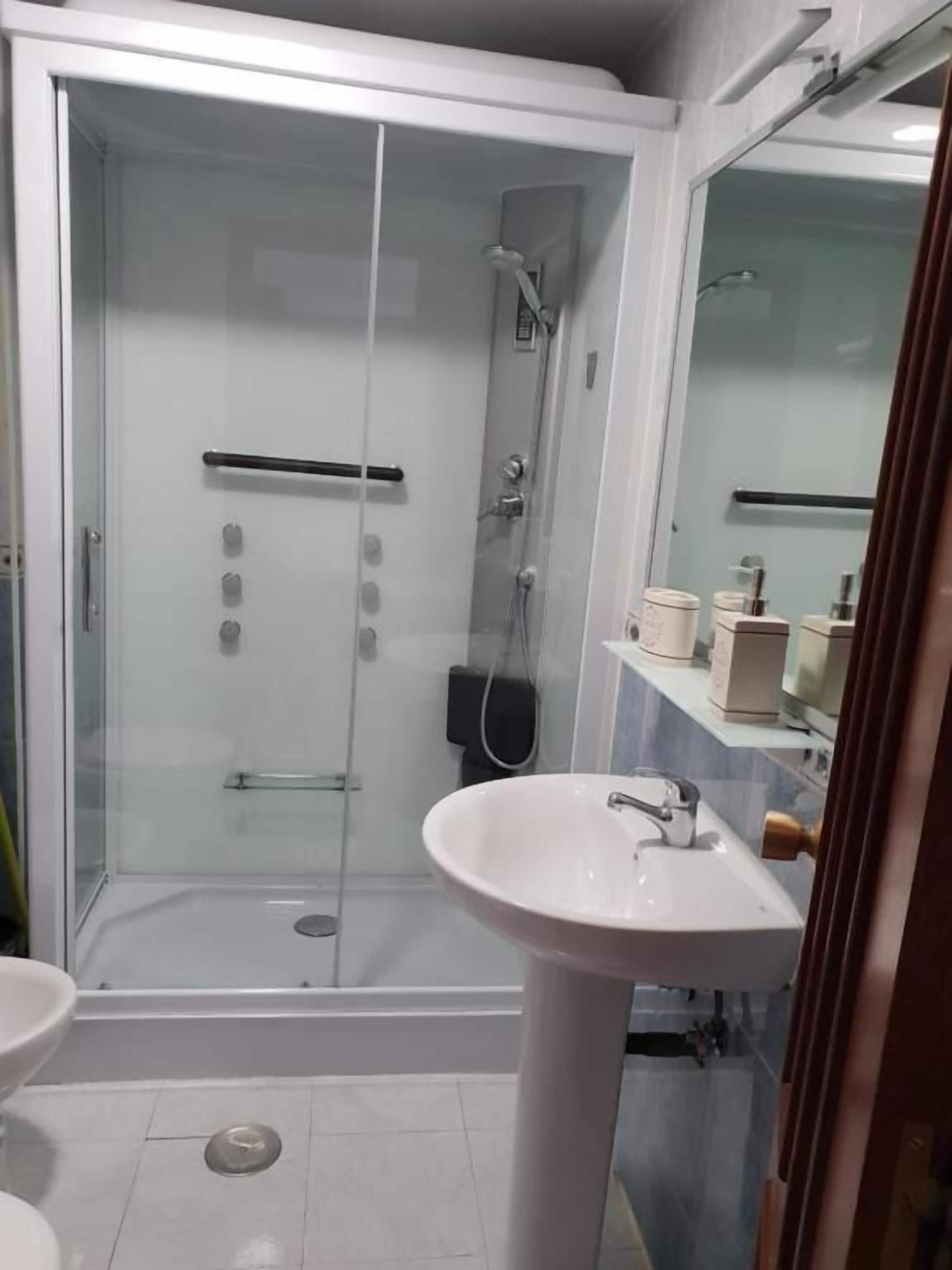 A bathroom with a glass-enclosed shower, a white sink, and a mirror.