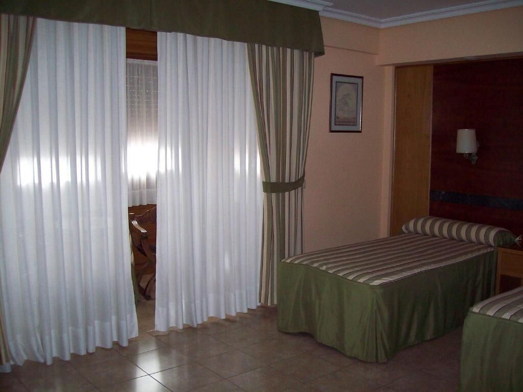 A hotel room with a bed, a chair, a table, and curtains.
