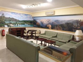 Un vestíbulo de hotel con un amplio mural panorámico, asientos verdes, una chimenea y un extintor.