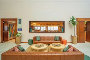 Un hall d’entrée avec un canapé en cuir, deux tables rondes, une grande fenêtre donnant sur un beau paysage et un panneau indiquant les heures d’ouverture.