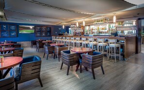 Un restaurant avec de nombreuses tables et chaises, un bar avec des bouteilles et des verres, et une image représentant un terrain de sport sur le mur.