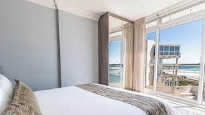 A bedroom with a large bed, a view of the beach, and a lifeguard tower.