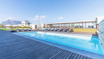 A rooftop pool with lounge chairs and a view of mountains.