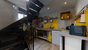 A modern kitchen with a black staircase, wooden cabinets, and a yellow accent wall. - Beautiful Coach House (Gloucester)