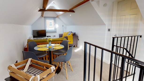 A cozy loft apartment with a dining area, a sofa, and a TV in the background. - Beautiful Coach House (Gloucester)