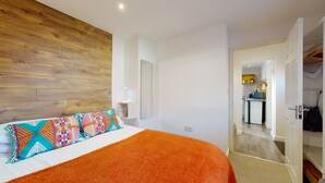 A bedroom with a wooden headboard, a bed with colorful pillows, and an orange rug. - Beautiful Coach House (Gloucester)