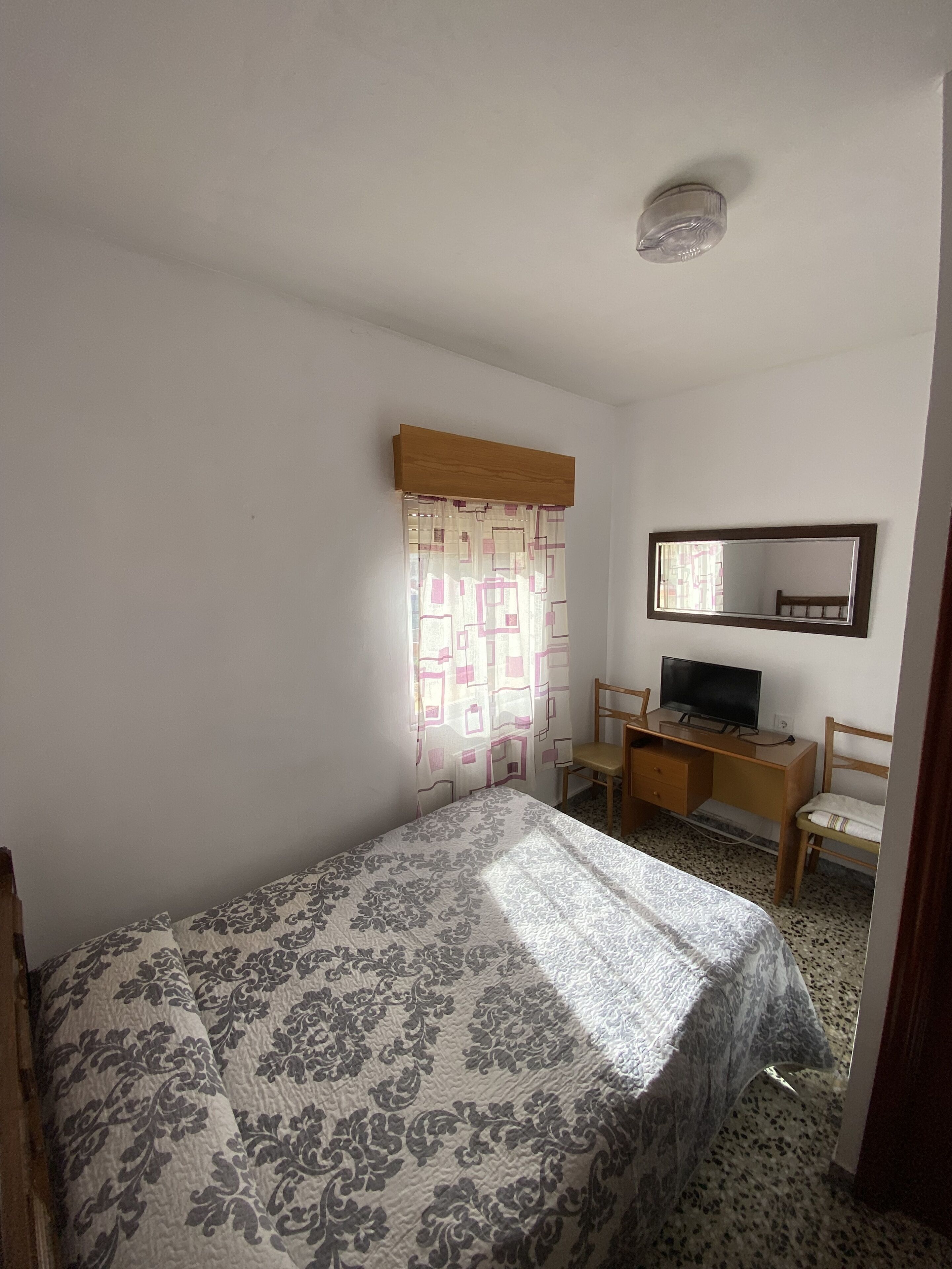 A bedroom with a bed, a desk with a chair, a television, and a mirror on the wall.