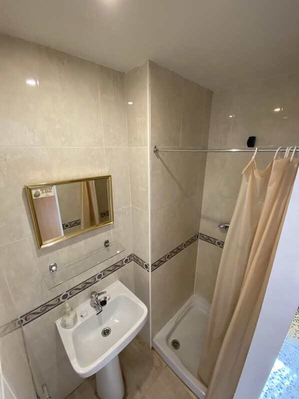 Un baño con ducha, lavamanos y espejo.