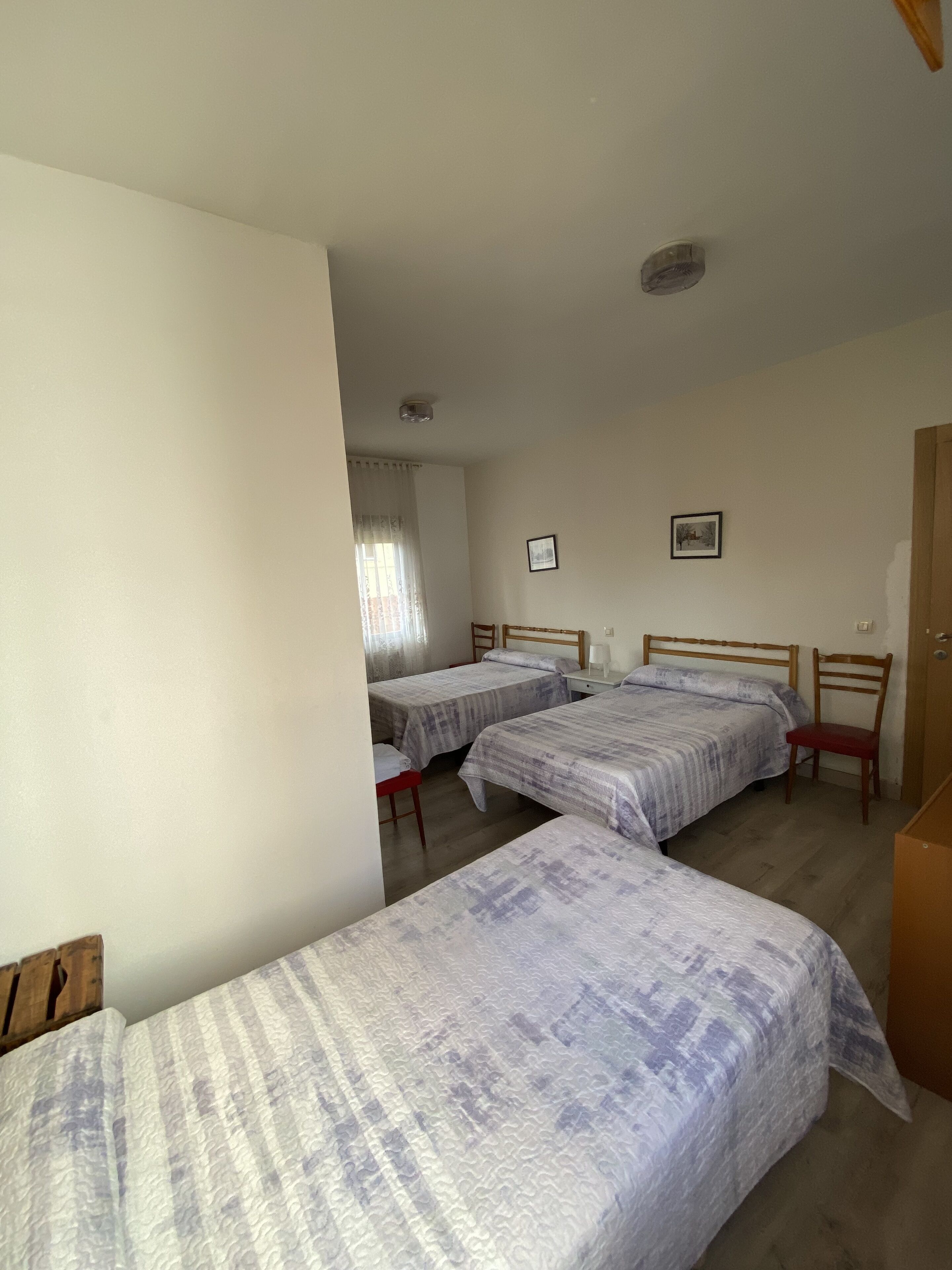 Una habitación con dos camas individuales, un armario de madera, una mesita y una ventana con cortinas.