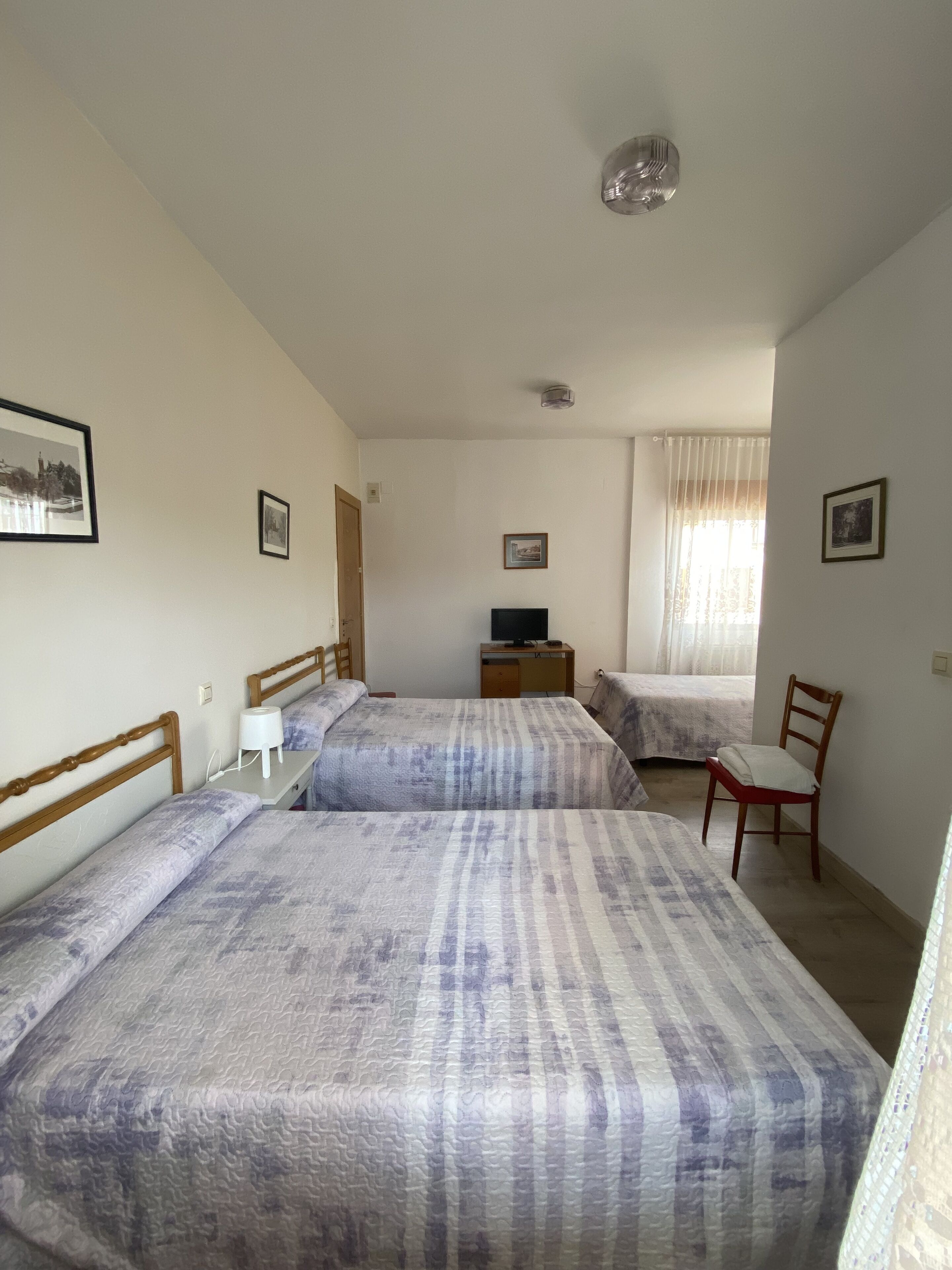 Ein Zimmer mit zwei Betten, einem Schreibtisch mit Computer, einem Stuhl und einem Fenster mit Vorhängen.