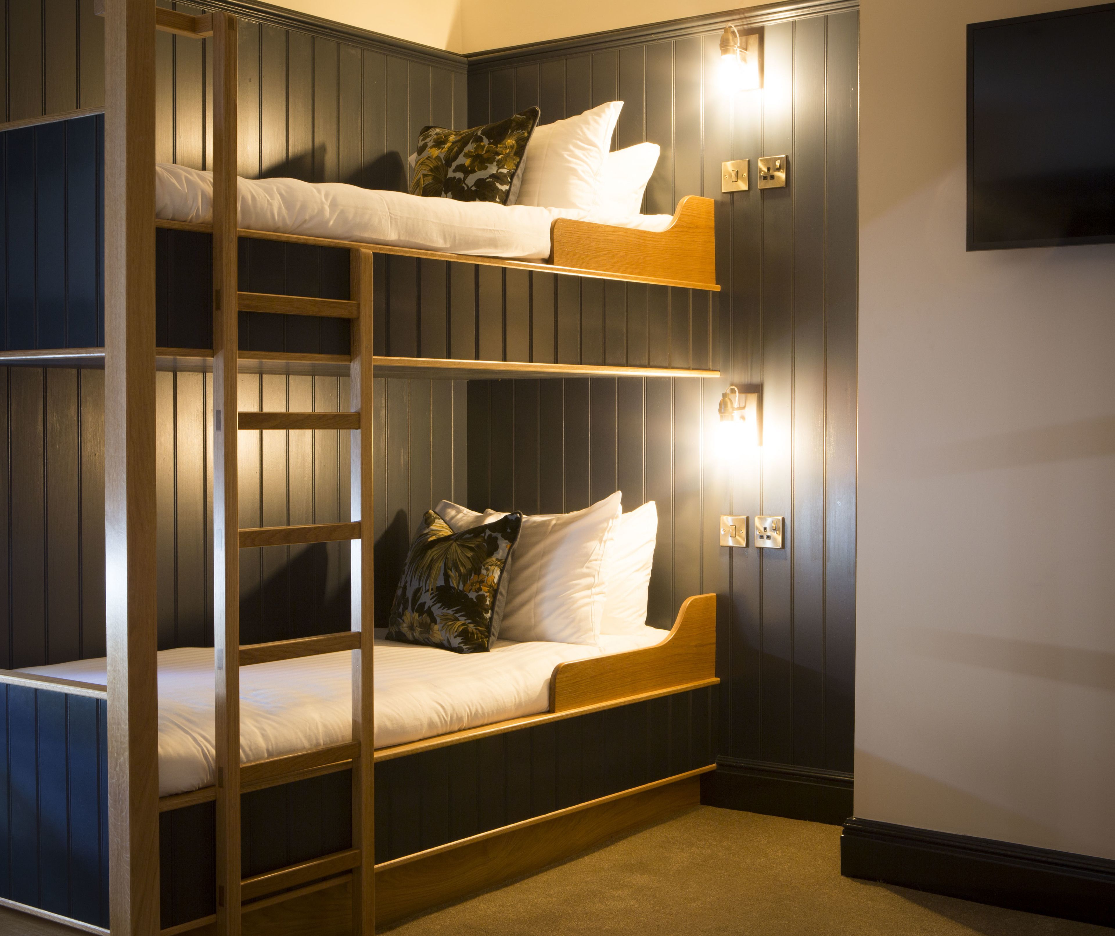 Een slaapkamer met stapelbedden, houten frames, witte beddengoed en een televisie aan de muur.