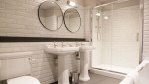 A modern bathroom with white marble tiles, two sinks, a toilet, and a glass-enclosed shower. - Wynnstay Arms (Wrexham)