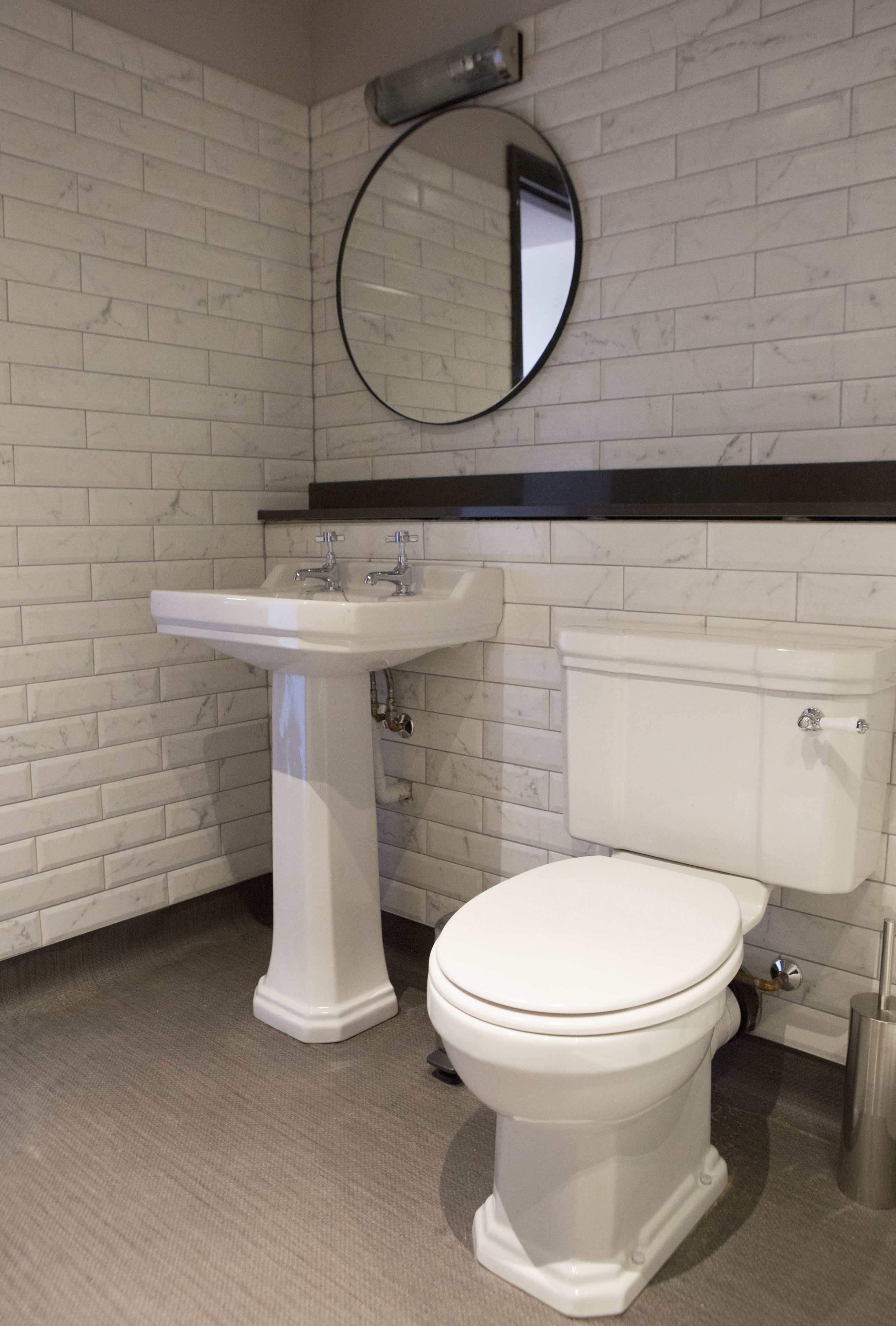 Een badkamer met een wit toilet, een wastafel op een voetstuk en een ronde spiegel aan de muur.