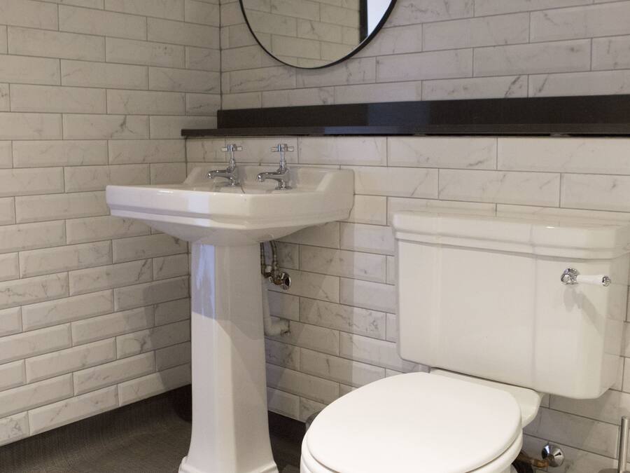 Un baño con inodoro blanco, lavamanos sobre pedestal y un espejo redondo en la pared.