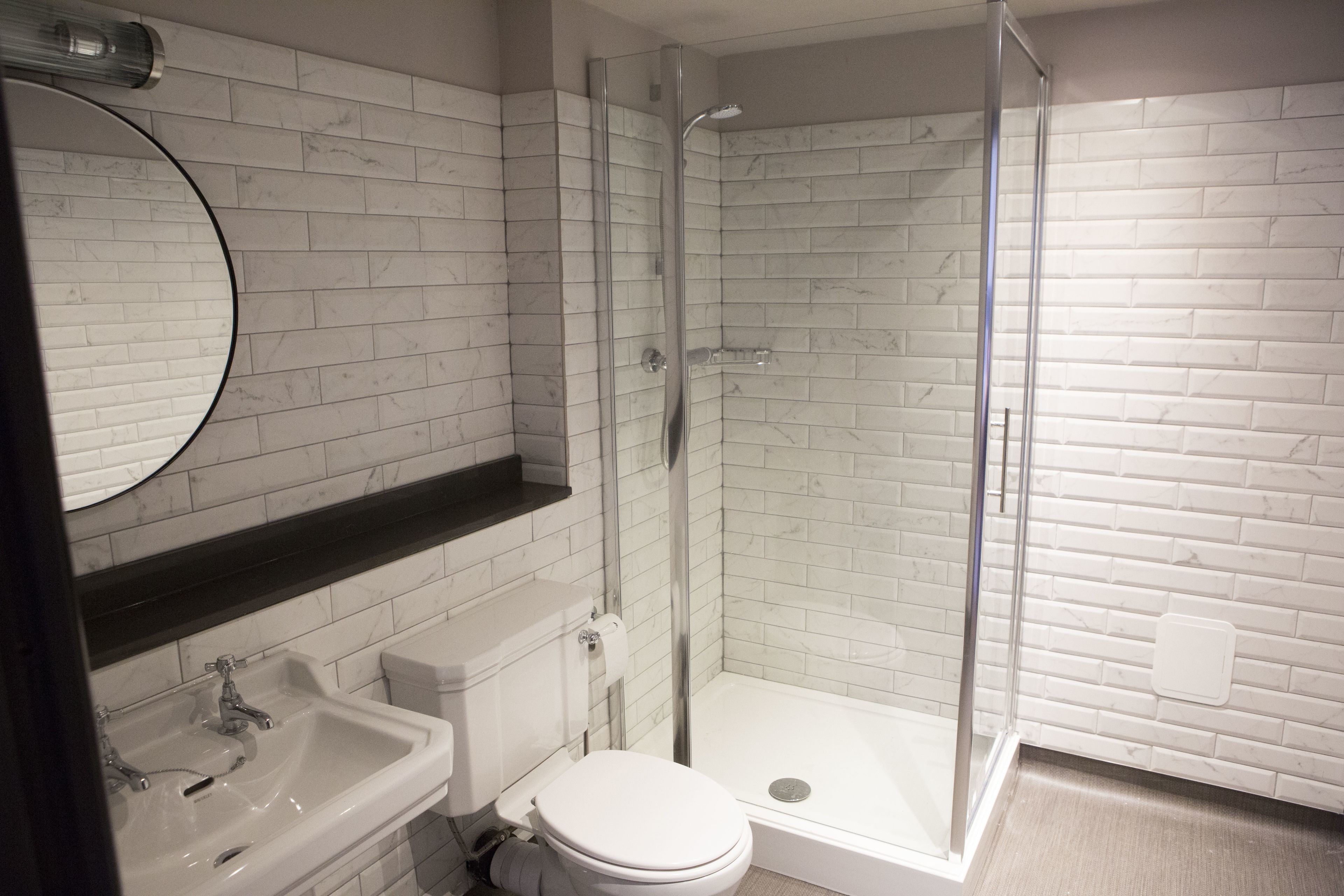 Un baño con inodoro blanco, lavamanos, ducha con puerta de vidrio y pared con azulejos de mármol.