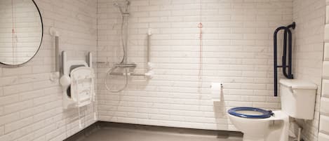 A bathroom with white brick walls, a white toilet with a blue seat, a showerhead, a hand dryer, and a mirror.
