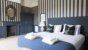 A neatly made bed with white linens and blue accents, a large mirror above the bed, and a dark blue wardrobe with a door. - Wynnstay Arms (Wrexham)