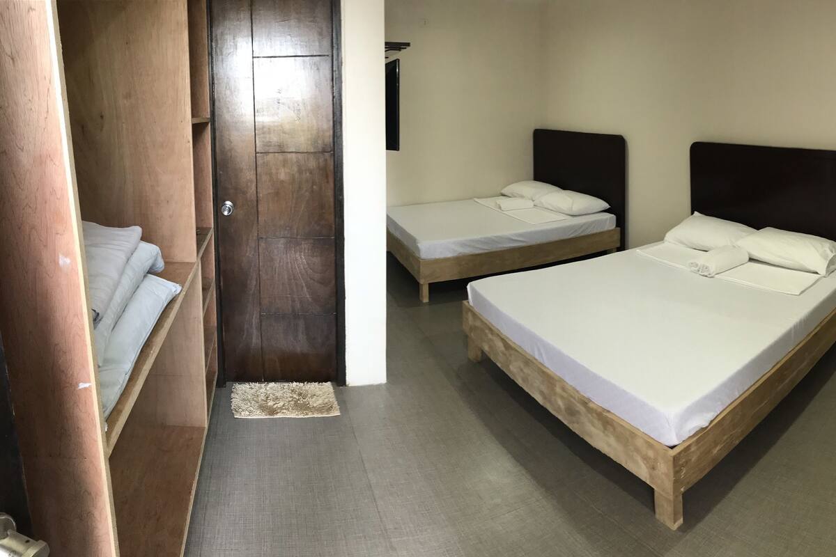 A room with two beds, a wooden wardrobe, and a door.