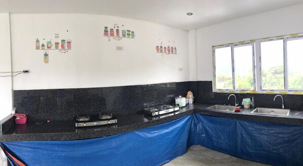 A kitchen with a black countertop, a gas stove, a sink, and a window with a view of greenery. - Seabreeze Beach Lodge (Nasugbu)