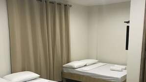 A hotel room with two single beds, each with white linens and pillows, a wooden floor, and beige curtains. - Seabreeze Beach Lodge (Nasugbu)
