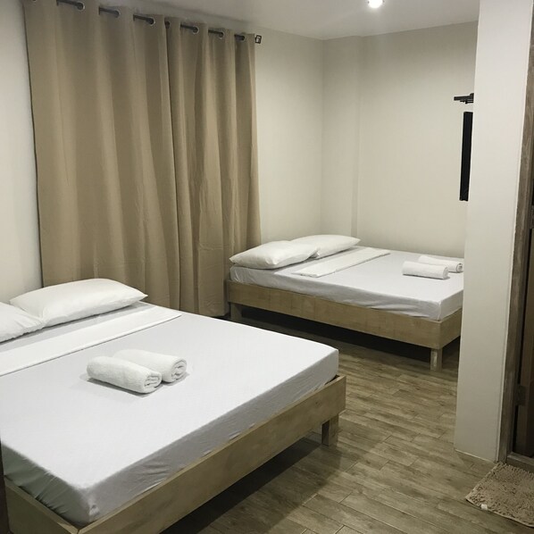 Habitación de hotel con dos camas individuales, cada una con ropa blanca y almohadas, suelo de madera y cortinas color beige.