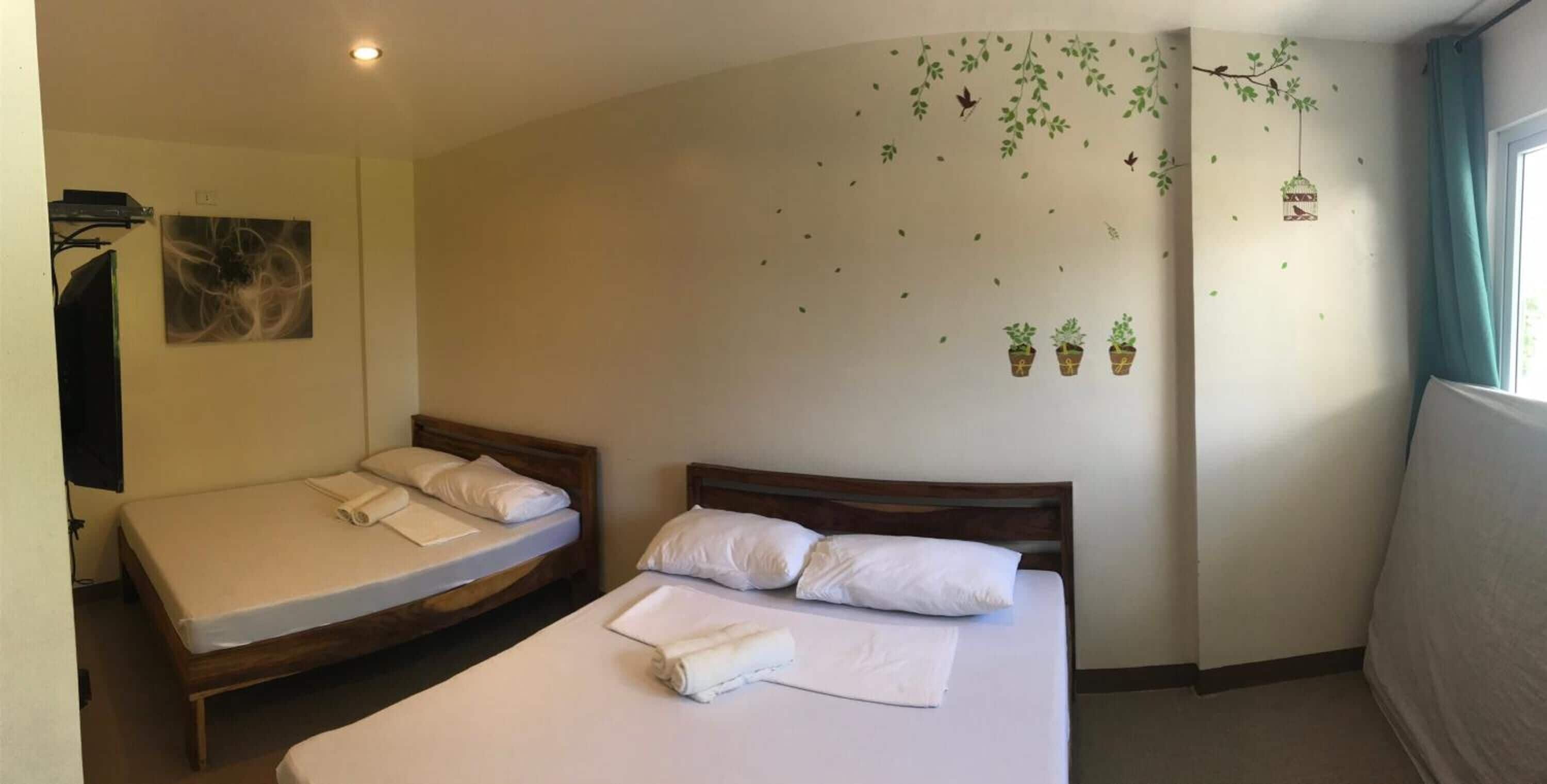Ein Hotelzimmer mit zwei Betten, einem Flachbildfernseher und einer Wanddekoration mit hängenden Pflanzen und Vögeln.