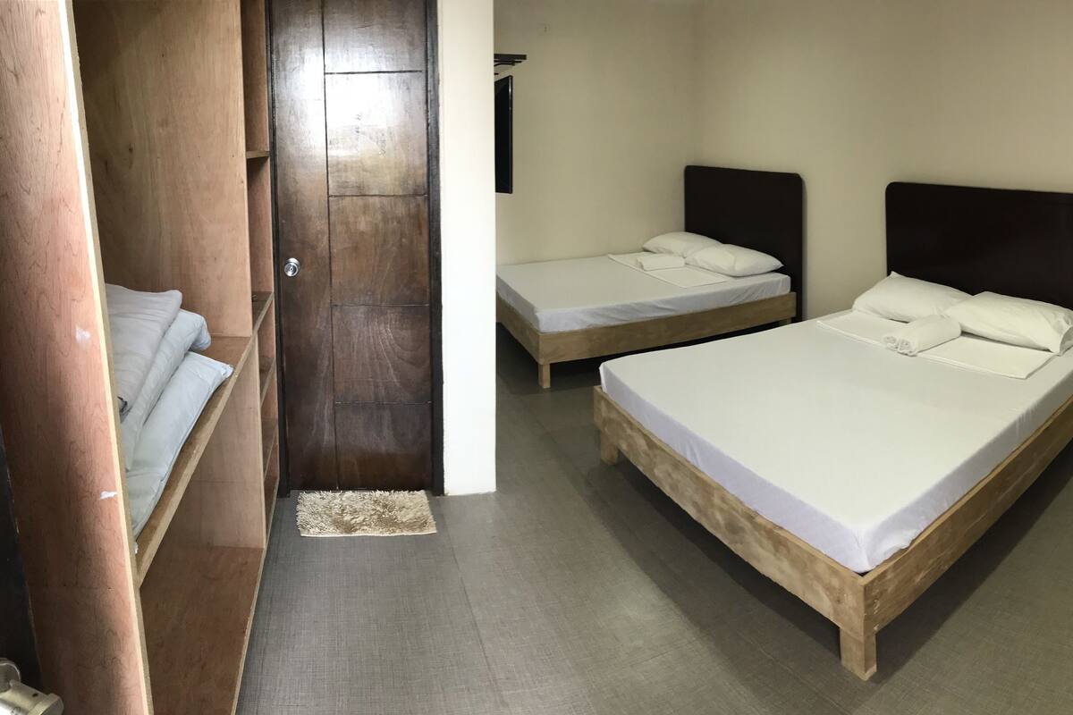 A room with two beds, a wooden wardrobe, and a small rug.