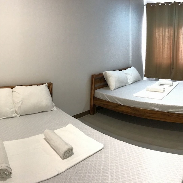 Ett hotellrum med två sängar, var och en med en träram och vitt sänglinne. Det finns handdukar på sängarna och ett fönster med gardiner.