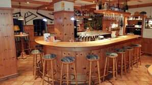 Eine Bar mit hölzernen Barhocker, einer Theke und verschiedenen Flaschen und Gläsern.