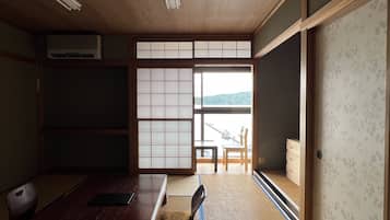 A traditional Japanese room with tatami flooring, a low table, and sliding doors leading to a balcony with a view of the sea.