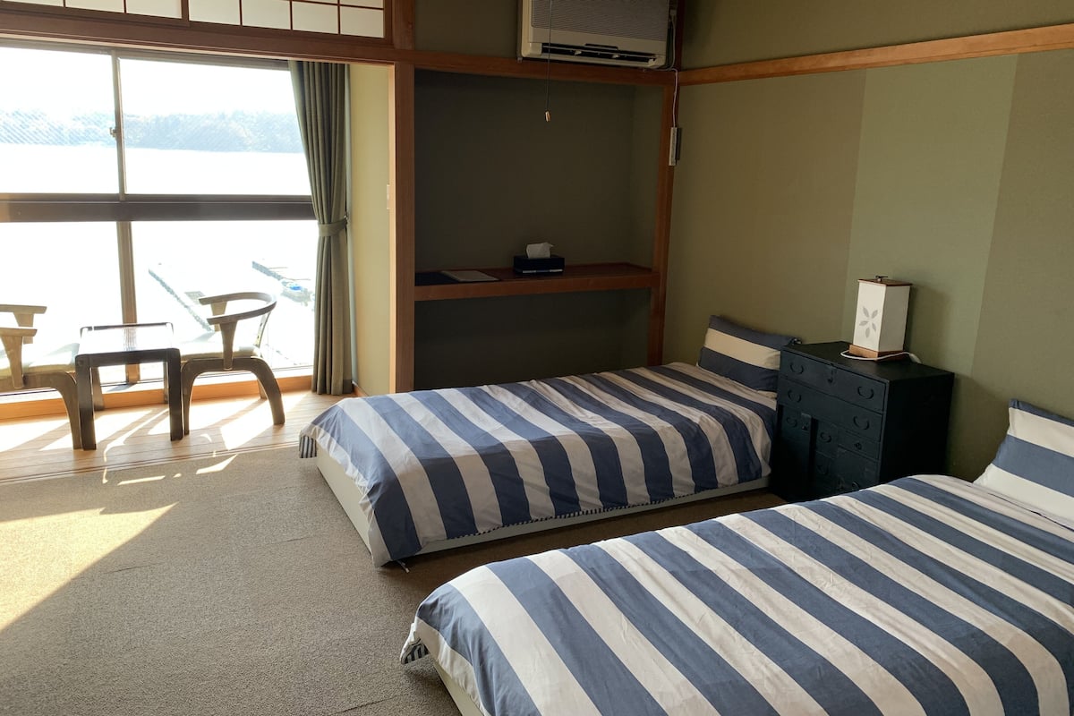 A room with two beds, a desk, and a chair. There is a window with a view of a body of water.