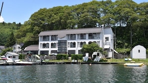 A large, multi-story building with a symmetrical facade, located beside a body of water with several boats docked. - Nojiri Lake Resort (Shinano)