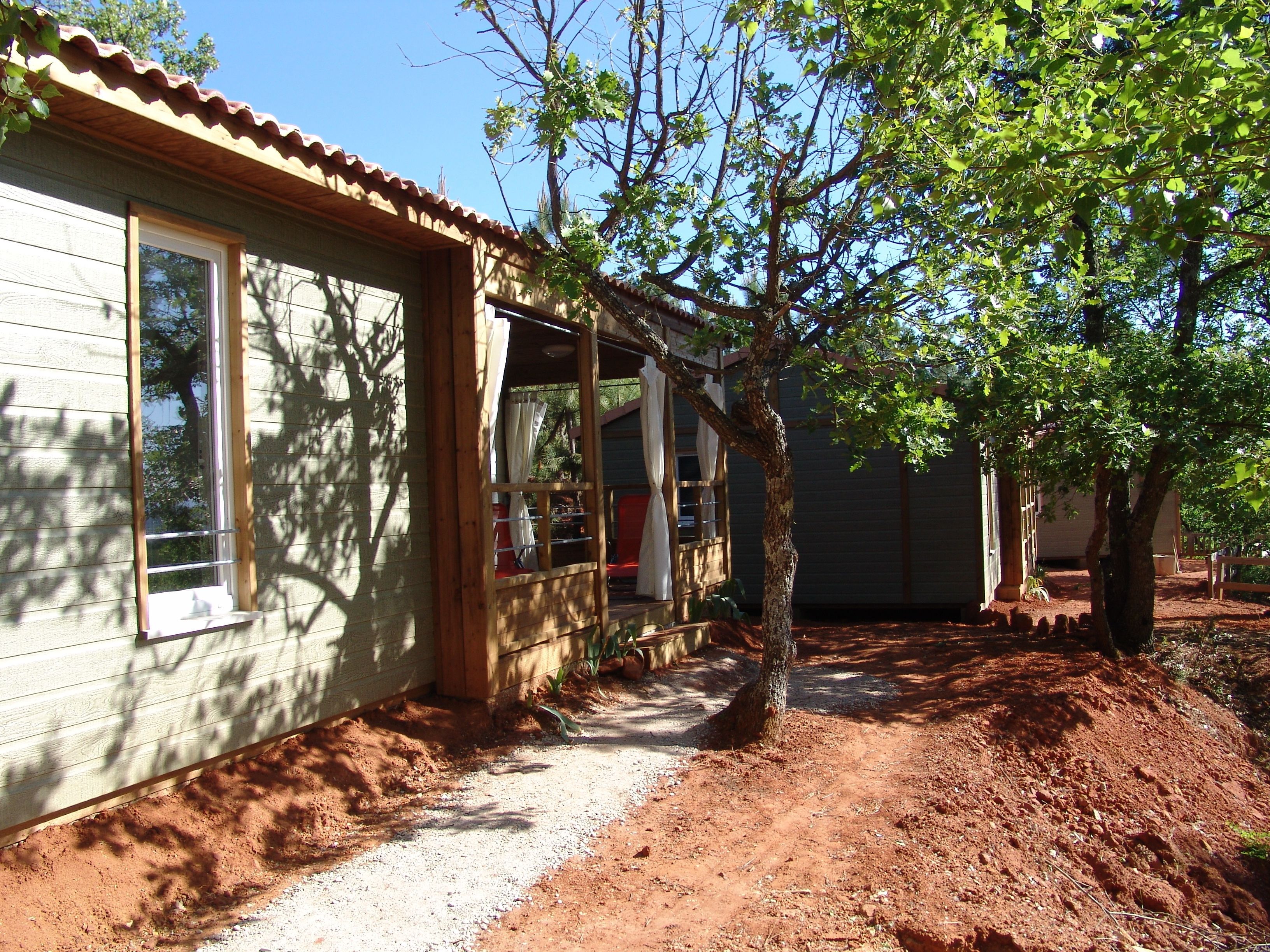 A house with a covered porch, a dirt path, and a tree in front.