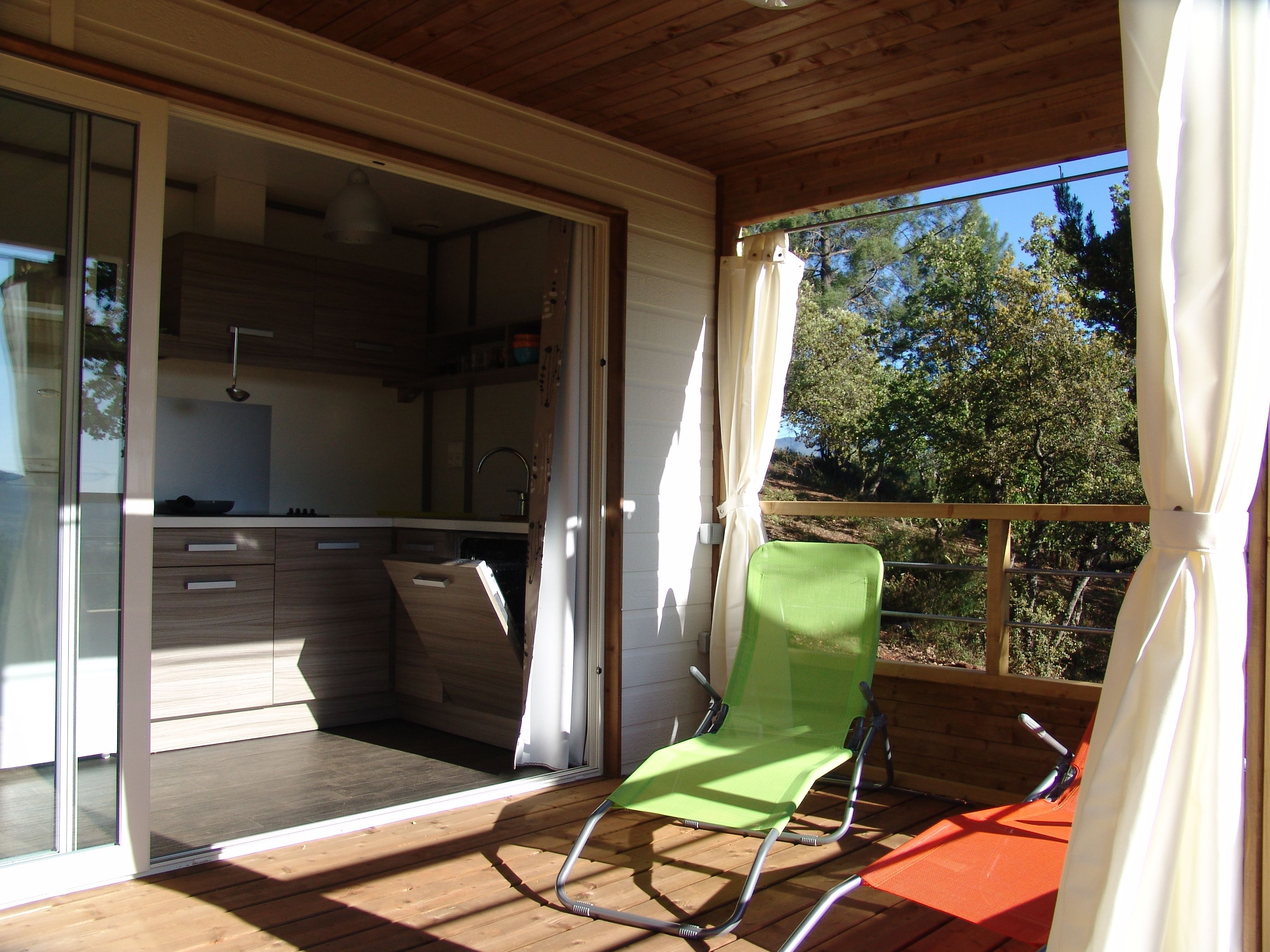 A balcony with a green chair, a wooden deck, and a kitchen area visible through glass doors.