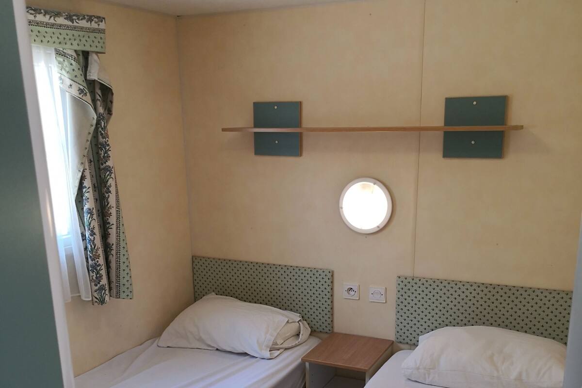Un alojamiento pequeño y de una sola habitación con dos camas individuales, una mesita y una lámpara fijada a la pared.
