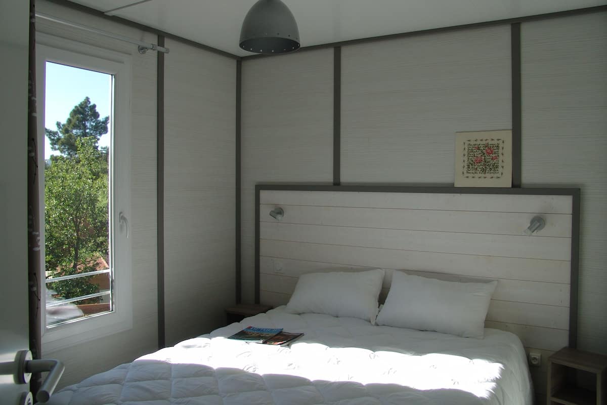 Un dormitorio con cama, ventana y lámpara en el techo.