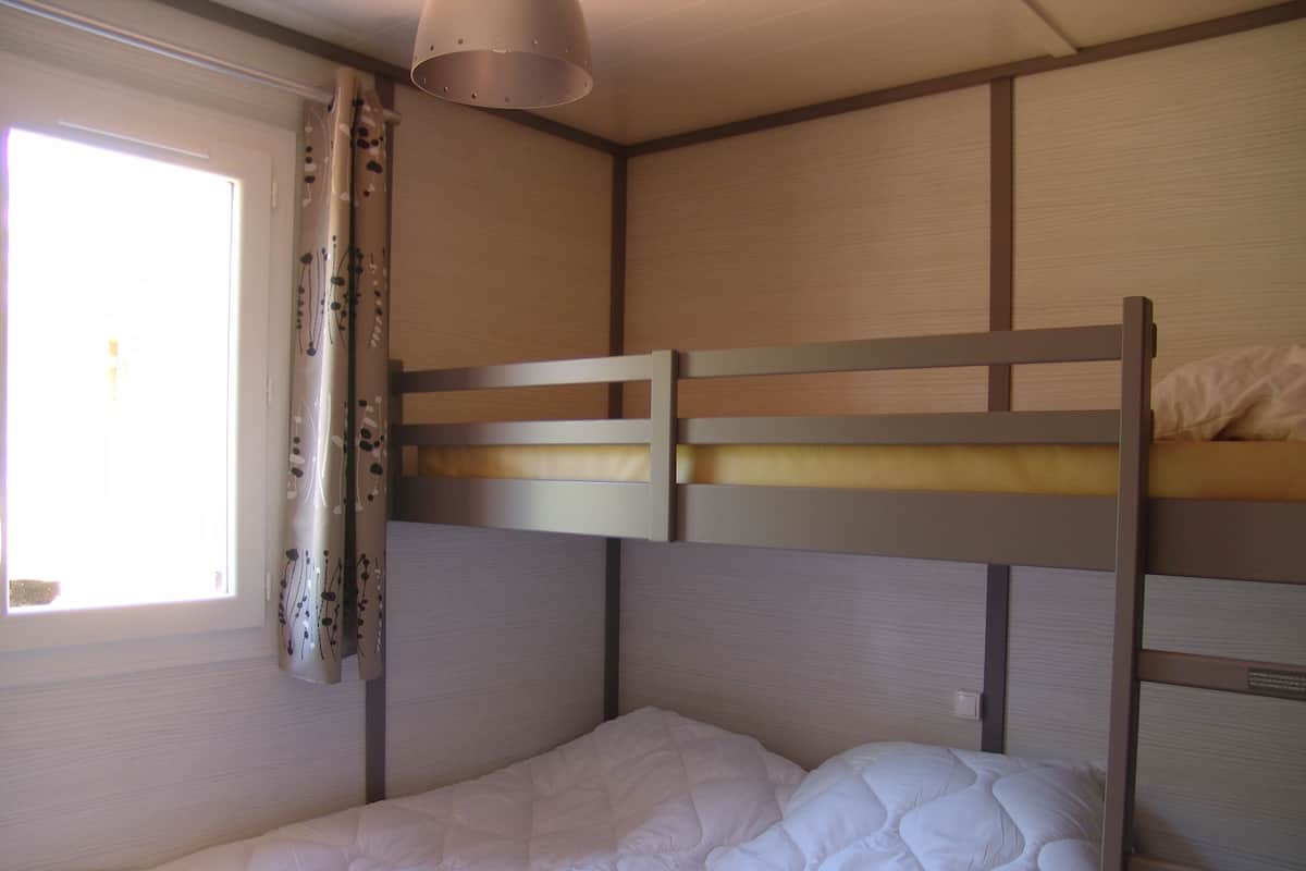 Dormitorio con literas, ventana, cortinas e iluminación colgante.