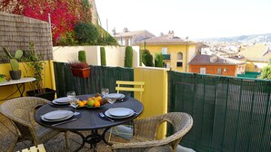 A round table set for four with wicker chairs, a yellow wall, and a view of a town in the background. - COLLINE DU CHATEAU AP4077 by RIVIERA HOLIDAY HOMES (Niza)