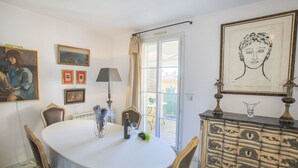A dining room with a round table, chairs, a lamp, a wine bottle, and a decorative cabinet. - COLLINE DU CHATEAU AP4077 by RIVIERA HOLIDAY HOMES (Niza)