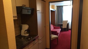 A compact hotel room with a kitchenette, a red-striped sofa, and a dining area with a table and chairs. - Gästehaus Albers (Cochem)