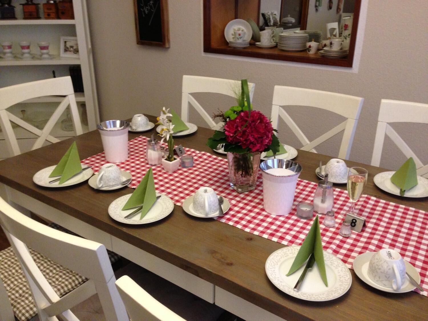 Een eettafel gedekt met borden, bestek en een rood-wit geruit tafelkleed.