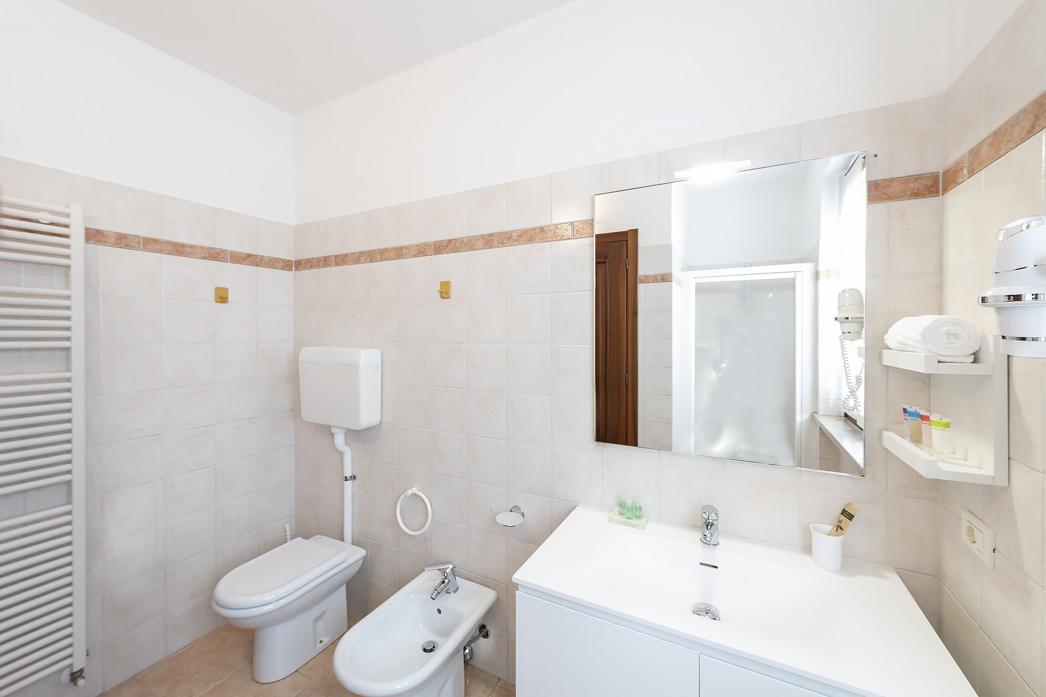 Een moderne badkamer met toilet, bidet, wastafel en spiegel.