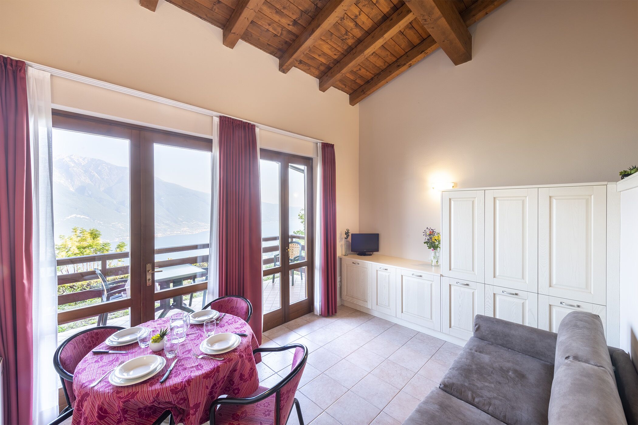 A dining area with a table set for four, a sofa, and a kitchen area with cabinets and a television.